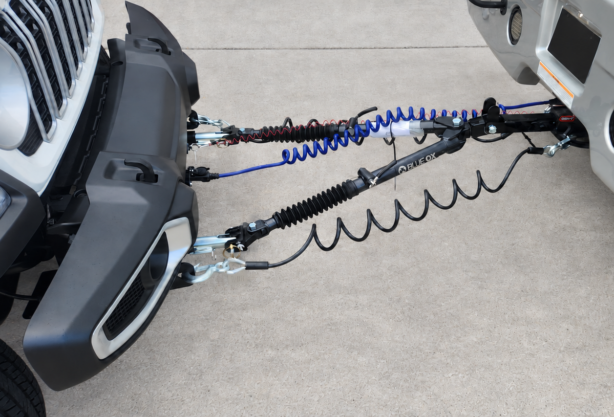 Blue Ox tow bar connecting a Jeep to a motorhome, with cables and wiring visible
